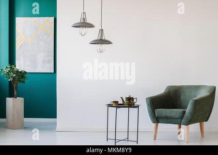 Moderno e di colore verde e bianco con camera teiera impostato sul tavolo, poltrona, pianta in un vaso, marmo sulla parete e lampade Foto Stock