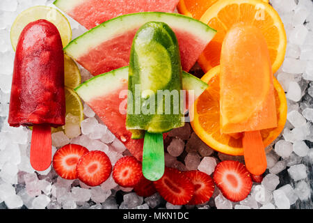 Angolo di alta vista di alcuni diversi fatti in casa pop di ghiaccio, realizzate con diversi succhi di frutta naturali e pezzi di frutta come cocomero, fragola, pisello Foto Stock