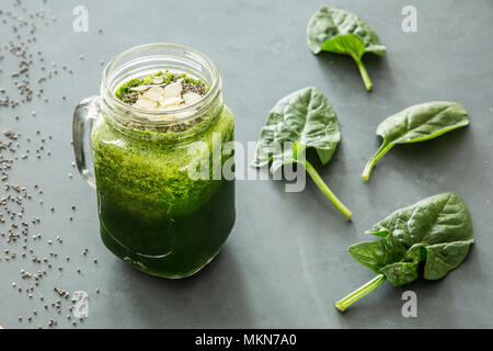 Sano frullato verde con spinaci e mandorle in un vaso accanto a foglie di spinaci giacente su una tabella di colore grigio Foto Stock