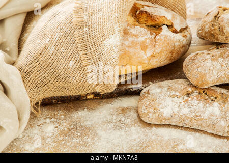 Close-up di pane e panini giacente su di un tavolo di legno con la farina su di esso in una panetteria Foto Stock