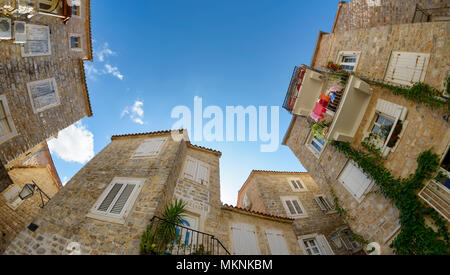 Piccola e pittoresca piazza con antiche case di pietra nella città vecchia di Budva, ampio angolo di vista dal basso verso l'alto con il cielo blu, Montenegro, Europa Balcanica Foto Stock
