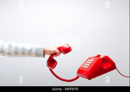 Mano che tiene il telefono, il braccio che indossa il verde e bianco, maglione rosso classico ricevitore telefonico, vecchio telefono su sfondo bianco battenti in weightlessnes Foto Stock