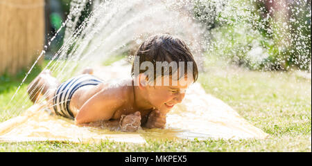 Ragazzo il raffreddamento con tubo flessibile da giardino, famiglia in background Foto Stock