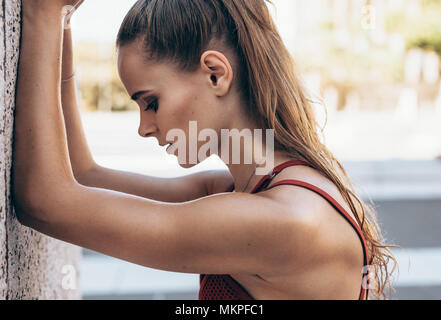 Close up stanco atleta femminile appoggiato su di un muro esterno. Vista di profilo di sportive in appoggio su una parete esterno dopo un allenamento. Foto Stock