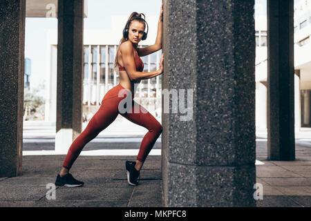 Lunghezza completa di un forte atleta femminile esercizio da una parete. La donna caucasica esercizio all'aperto nella città. Foto Stock