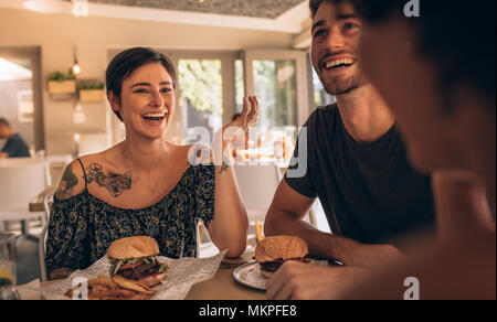 Allegro giovane donna che parla con i suoi amici al ristorante con gli hamburger sul tavolo. Amici appendere fuori a un cafe'. Foto Stock