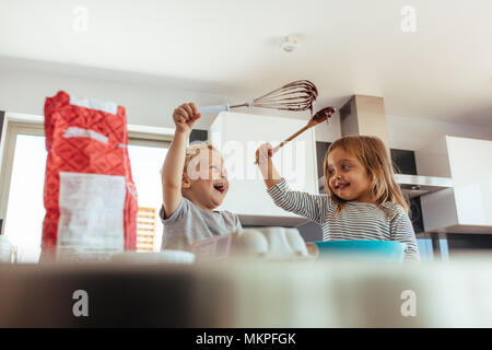 Carino piccolo ragazzo e ragazza con frusta e la spatola per divertirsi durante la cottura in cucina. Kids godendo rendendo torta in cucina. Foto Stock