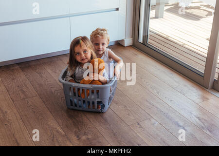 Giovane e bella bambini seduti in un cestello di lavaggio a casa. Bambina tenendo un orsacchiotto di peluche e suo fratello gioca in casa. Foto Stock