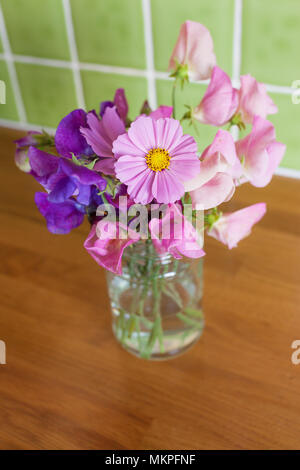 Miscelati, fresco mazzetto di fiori da giardino in un recipiente su un tavolo da cucina. Profondità di campo ridotta con focus sul cosmo fiore. Foto Stock