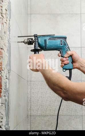 Il lavoratore in possesso di un trapano e fare un foro nella parete. Foto Stock