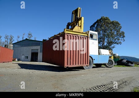 Un enorme carrello elevatore si sposta a 20 piedi di contenitore di spedizione nel cortile di una fabbrica di grandi dimensioni. Foto Stock