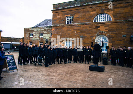Coro rock cantando in Delafre Abbey Northampton UK cantando carols natalizi in cortile vestito di nero in casa di neve con finestre ad arco direttore Foto Stock