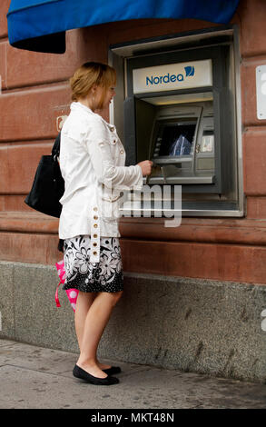 Una giovane donna bionda tenendo fuori i soldi da un bancomat appartenenti alla Banca Nordea nella città di Uppsala, Svezia. Foto Stock