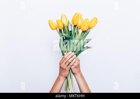 Mani femminili con manicure tenere un bouquet di tulipani gialli su sfondo bianco Foto Stock