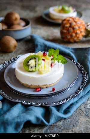 Delizioso mini crudi cheesecake guarnita con ananas, kiwi e melograno Foto Stock
