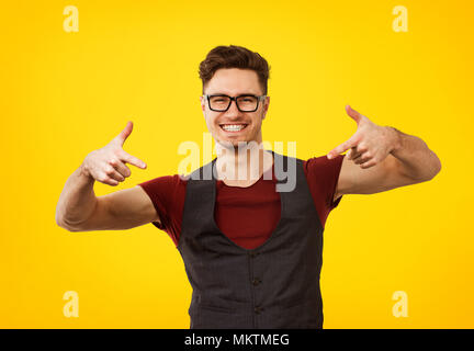 Ritratto di giovane uomo in elegante abito fresco e i bicchieri che pongono espressamente su sfondo giallo Foto Stock