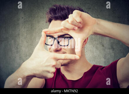 Giovane uomo rendendo il telaio con le mani la creazione di shot e guardando la fotocamera. Foto Stock