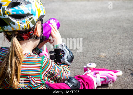 Un ragazzo e una ragazza che indossa roller-blade seduta e di mangiare e di bere acqua minerale. Foto Stock