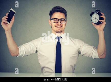 Contenuto di giovane lavoratore titolare smartphone e sveglia di trascorrere del tempo con gadget al lavoro. Foto Stock