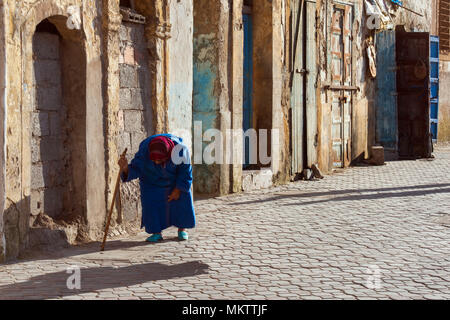 Odf piegate donna cammina con una bacchetta lungo le antiche mura della medina di Essaouira, Marocco. Foto Stock
