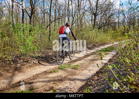 Un giovane uomo in abbigliamento sportivo giostre di una bicicletta su strada nella foresta. Foto Stock