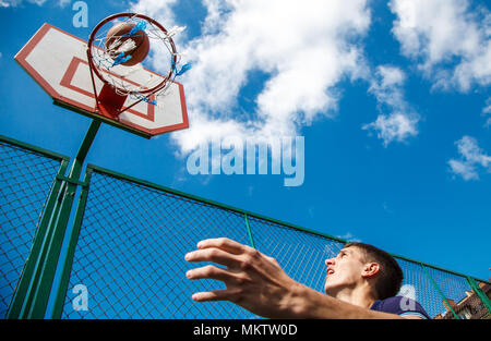 Giovane uomo giocare a basket nel cortile su una soleggiata giornata estiva Foto Stock