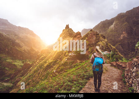 Ragazza camminare verso il basso lungo il percorso di trekking per la verdeggiante valle Xo-Xo. Luce calda del sole seable su horizont. Santo Antao Isola Capo Verde Foto Stock