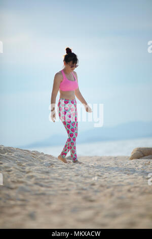 Donna che indossa lo sport adatto a camminare sulla spiaggia di sabbia bianca Foto Stock