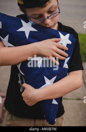 Un ragazzo giovane azienda ripiegata di bandiera americana. Foto Stock