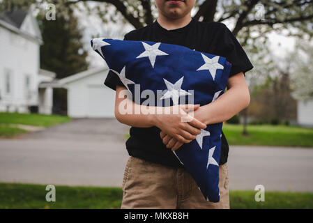 Un ragazzo giovane azienda ripiegata di bandiera americana. Foto Stock