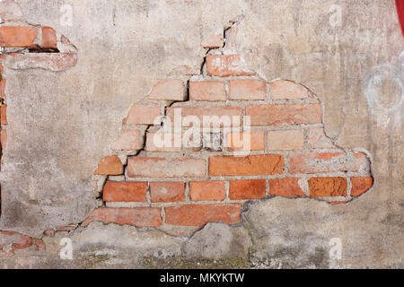 Muro di mattoni che necessitano di riparazioni con il crack e intonaco danneggiato. Foto Stock