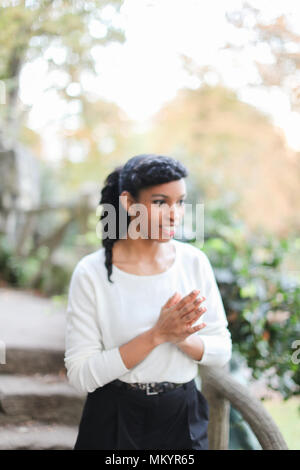 Nero giovane ragazza piuttosto che indossa camicia bianca e pantaloni in scale di pietra dello sfondo. Concetto di eleganza Afro American persona e bellezza naturale. Foto Stock