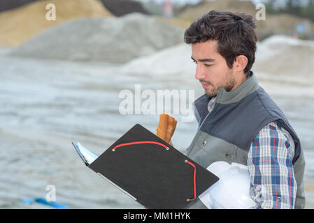 Uomo che guarda un file, mangiare panino Foto Stock