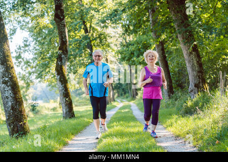 Due anziani attivi con uno stile di vita salutare sorridendo durante il jogging insieme Foto Stock