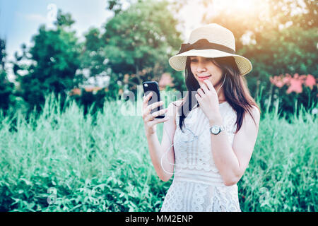 La bellezza delle donne tenendo lo smartphone e ascolto di musica mediante auricolare,le donne nel tempo felice che la luce del sole e il sorriso,shopping online tramite internet mobile Foto Stock