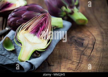 Freschi di carciofi viola sul scuri in legno rustico sfondo con fette di limone Foto Stock