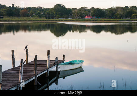 Dock in legno e una piccola barca in un lago di sunrise Foto Stock