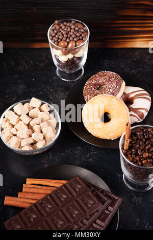 Vetro con i chicchi di caffè accanto a tavolette di cioccolato, ciambelle, lo zucchero di canna e di altro vetro con arachidi in cioccolato Foto Stock