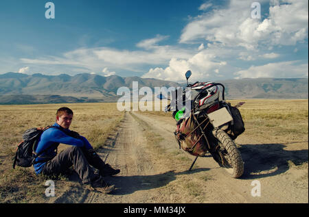 Motociclo traveler uomo seduto su extreme rocky steppa percorso stradale in montagna su un altopiano nel torbido meteo su uno sfondo di colline montagne di Altai S Foto Stock