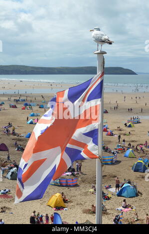 Union Jack flag con seagull appollaiato sulla bandiera polo a Woolacombe Beach in una calda giornata estiva con un sacco di persone in Devon England Foto Stock