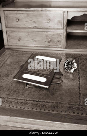 Passaporto britannico su un portafoglio in pelle con un orologio rolex su un'antica scrivania in legno, in seppia Foto Stock