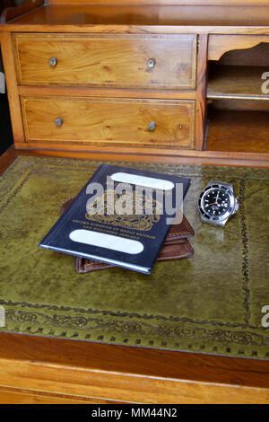 Passaporto britannico su un portafoglio in pelle con un orologio rolex su un'antica scrivania in legno Foto Stock