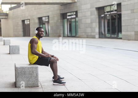 La felicità afro uomo seduto, toothy smaling dopo allenamento. Colpo all'aperto, la mattina. Primavera o estate Foto Stock