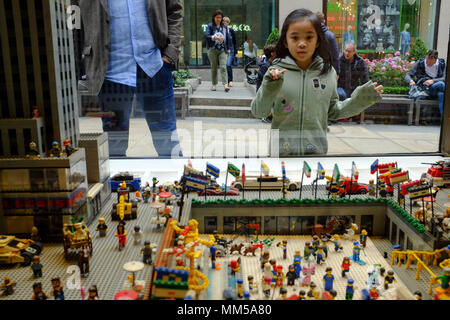 Una giovane ragazza asiatica guarda attraverso la finestra del negozio Lego in corrispondenza di un visualizzatore del Rockefeller Center di New York City il 6 maggio 2018. Foto Stock