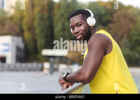 Ritratto di bella pelle nera uomo, ascolta musica dopo l'allenamento. Sfondo sfocato. Colpo all'aperto, la mattina. Primavera o estate Foto Stock