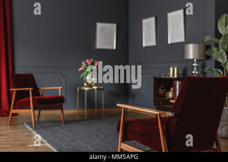 Close-up di legno rosso poltrona in grigio spazioso salotto interno con manifesti in sfondo sfocato Foto Stock