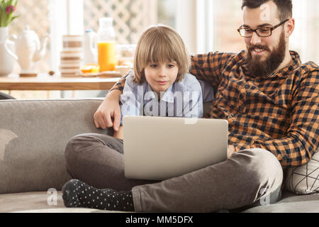 Felice padre e figlio guardando un film su un portatile, seduto su un divano a casa Foto Stock