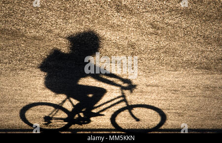 Defocalizzata sfocata ombra silhouette di una persona giovane in sella a una moto sul tramonto shiny strada asfaltata Foto Stock