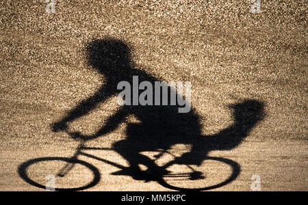 Defocalizzata sfocata ombra silhouette di un padre in sella a una moto con il suo bimbo bambino sul sedile posteriore sul tramonto shiny strada asfaltata Foto Stock