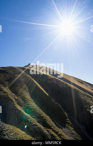 Silhouette di montagna erbosa con cottage sulla sua parte superiore Foto Stock